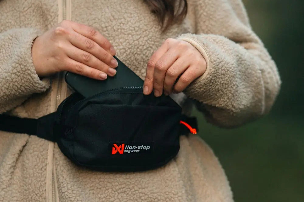 A woman placing her phone into the Trail Quest Storage Pack, with a sherpa jacket on.