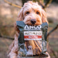 Dog holding a bag of Anco Naturals Bully Sticks.