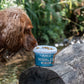 Lifestyle image of the Anco Nibbles on  top of a tree log, with a dog sniffing the treats.