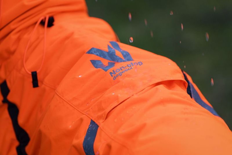 Lifestyle image of the Orange Fjord Overall, with Non-stop branding and rain falling on the coat.