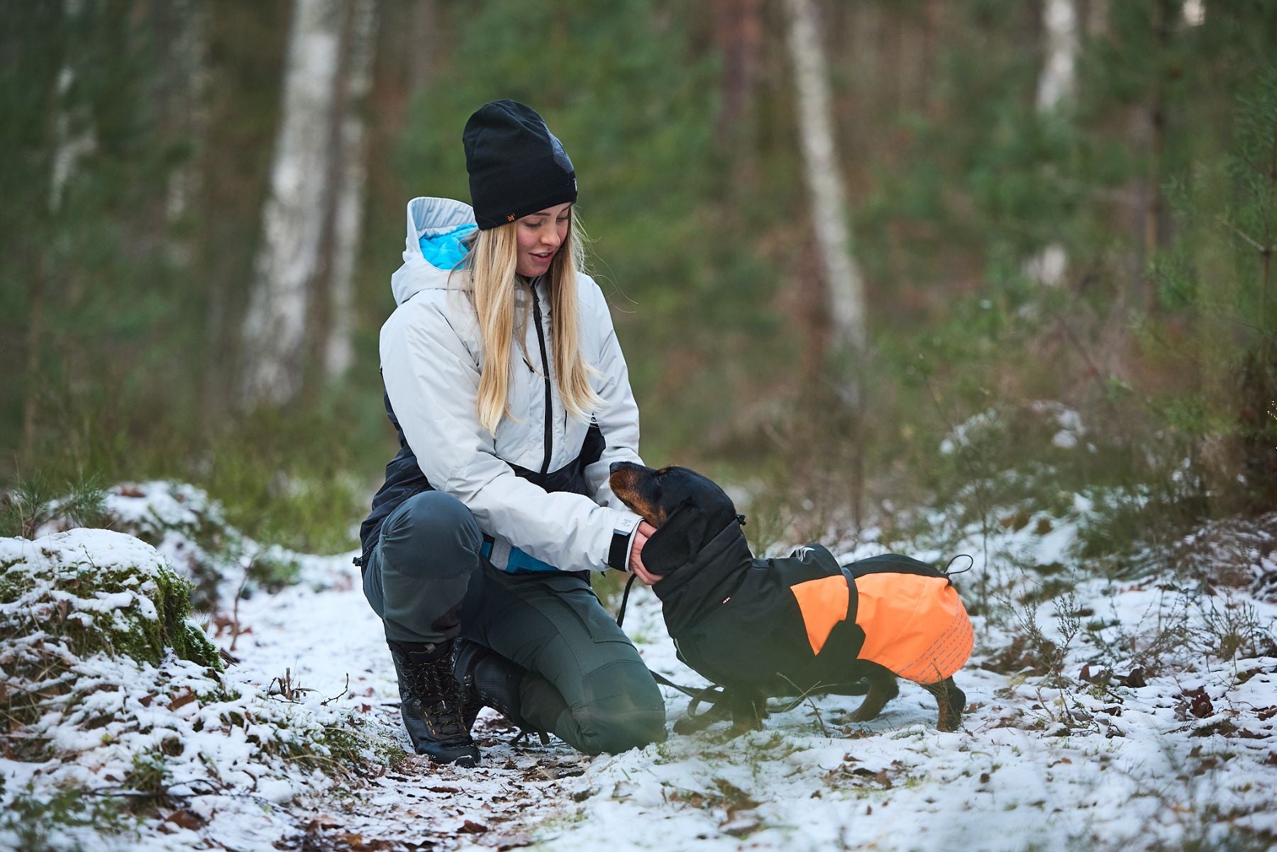 Lifestyle image of the Glacier Jacket, with a woman kneeled down in the snow next to her dog.