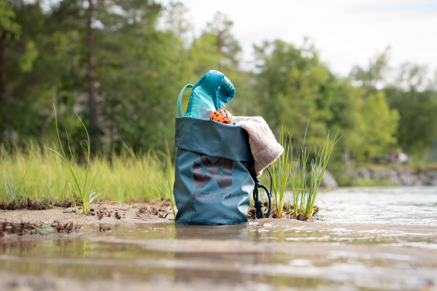 The Multiuse Bag carrying towels and toys, in a river environment.