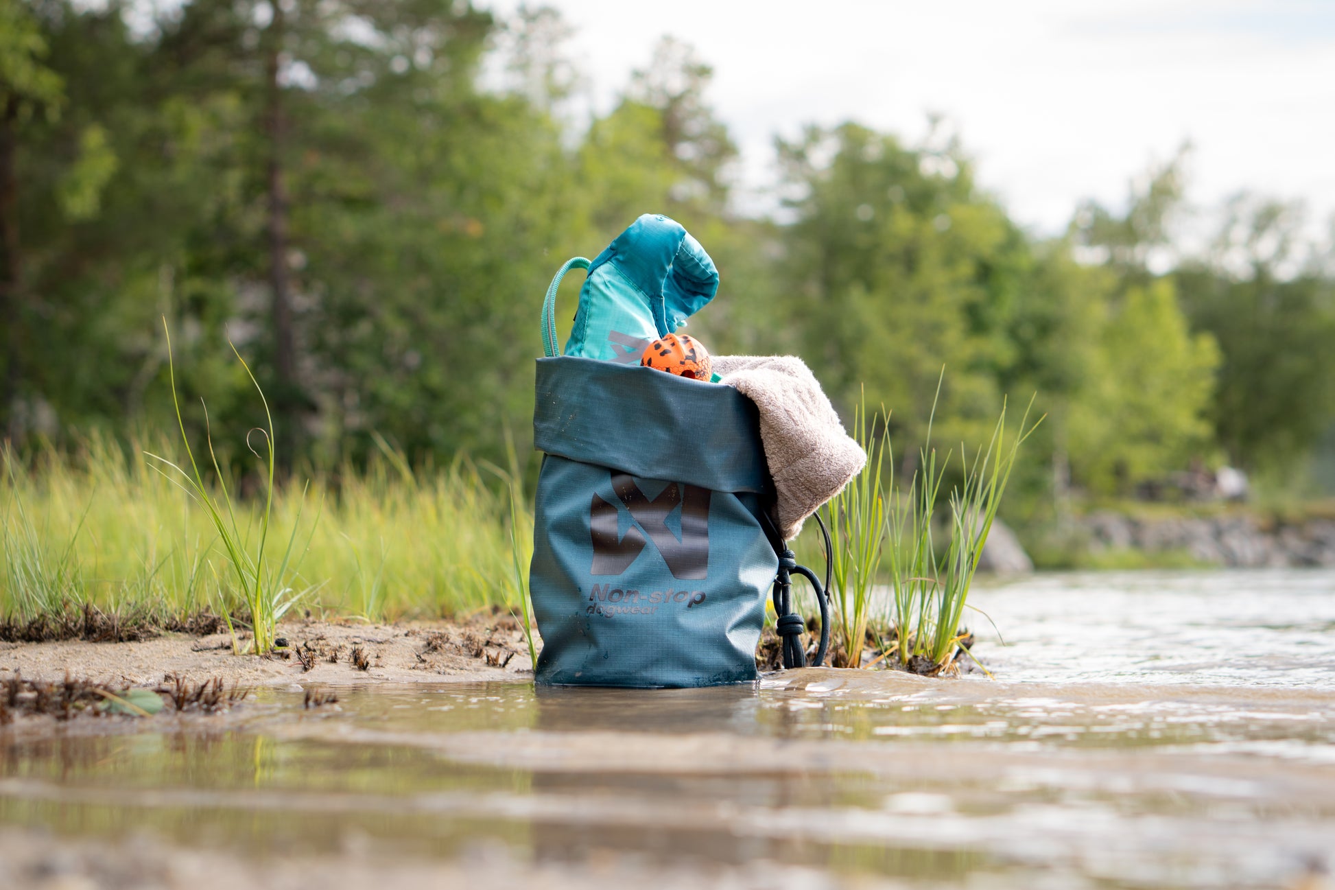 The Multiuse Bag carrying towels and toys, in a river environment.