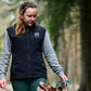 Woman walking a dog on a path in a forest, holding a dog lead while her dog looks up at her.