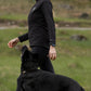 Woman walking a black dog in a forested area.