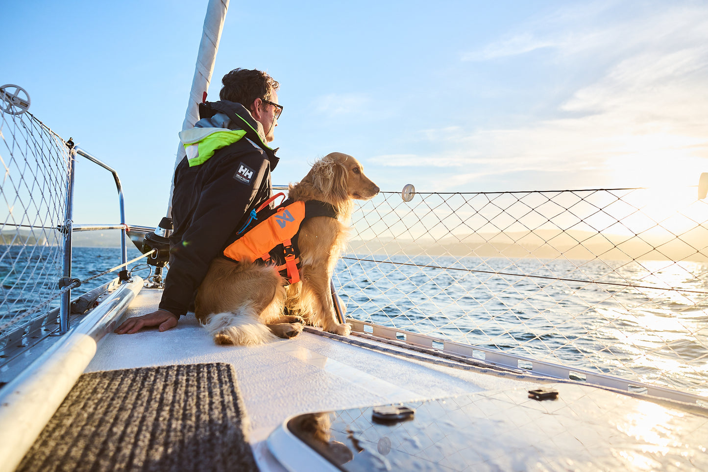 Lifestyle image of the Protector Life Jacket, showing a dog sitting on the end of a boat with a person, looking out into the ocean.
