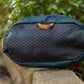 Lifestyle image of the Rachel Pohl Trail Quest Storage Pack, on a brick wall with a leafy backdrop.
