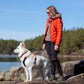 Lifestyle image of the Rope Lead, showing a white dog wearing a harness and a lady wearing an orange coat, standing on a rock with a river background.