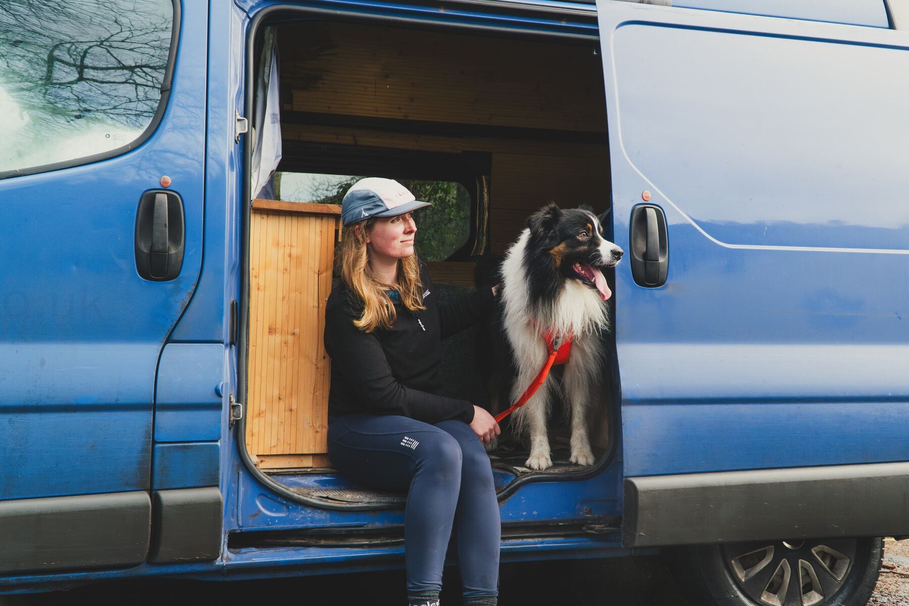 Lifestyle image of the Front Range Harness, with an owner sat beside a dog in a campervan, holding a lead.