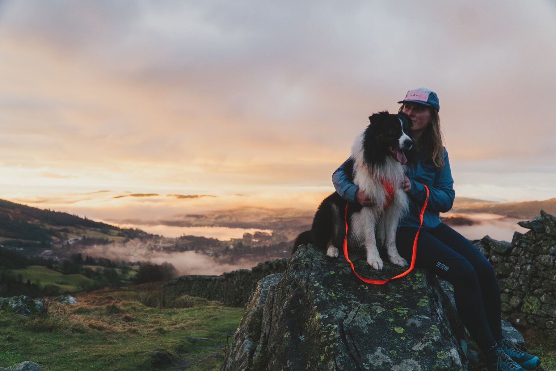 Lifestyle image of the Front Range Lead, clipped into a dog's harness while the dog and their owner sit on the rock of a peak.
