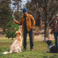 Lifestyle image of the Gnawt-a-Stick being held above 2 dogs, while they wait for it to be thrown. 2 people are dressed in warm clothing, with a park background.