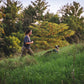 Lifestyle image of the Hi & Light Harness, with a dog walking ahead of a woman through the grass.