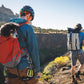 Lifestyle image of the Hitch Hiker Carrier, showing a dog on the back of someone doing a hike, with other people hiking alongside some rough terrain.