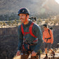 Lifestyle image of the Hitch Hiker Carrier, showing a dog on the back of someone doing a hike, with other people hiking alongside some rough terrain.
