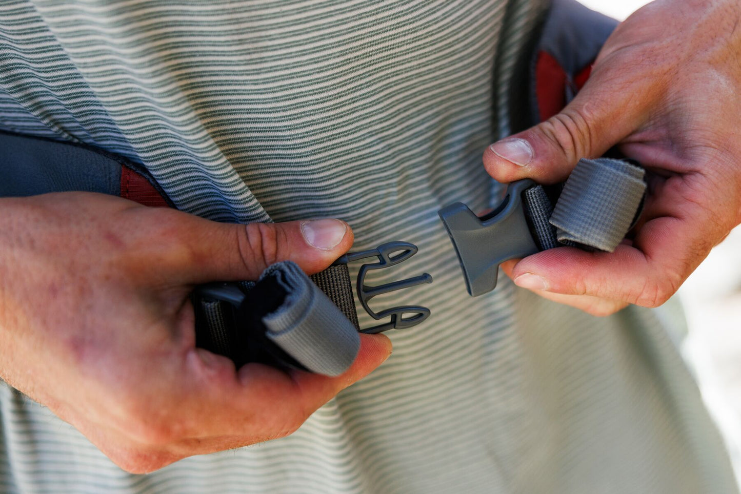 Lifestyle image of the Hitch Hiker Carrier, showing two hands buckling up the waist strap.