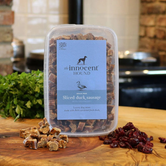 The Innocent Hound Sliced Duck Sausage Treats are displayed on a wooden surface with treats and ingredients.