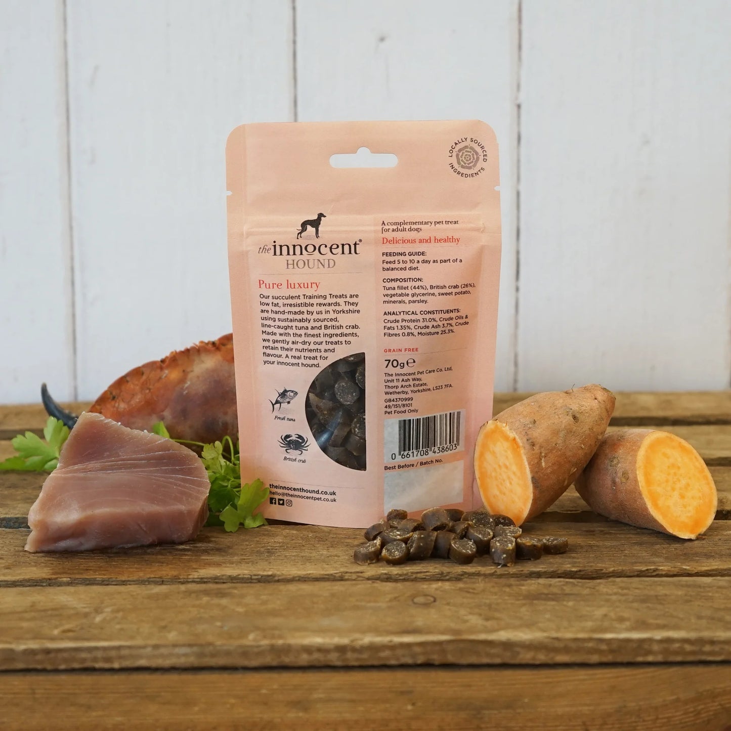 The back of the Innocent Hound Training Crab and Tuna Treats packets are displayed on a wooden surface with treats and ingredients.