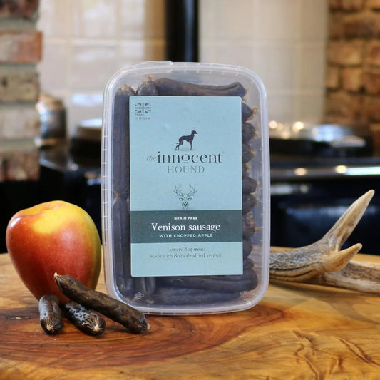 The Innocent Hound Venison Sausage Treats are displayed on a wooden surface with treats and ingredients.