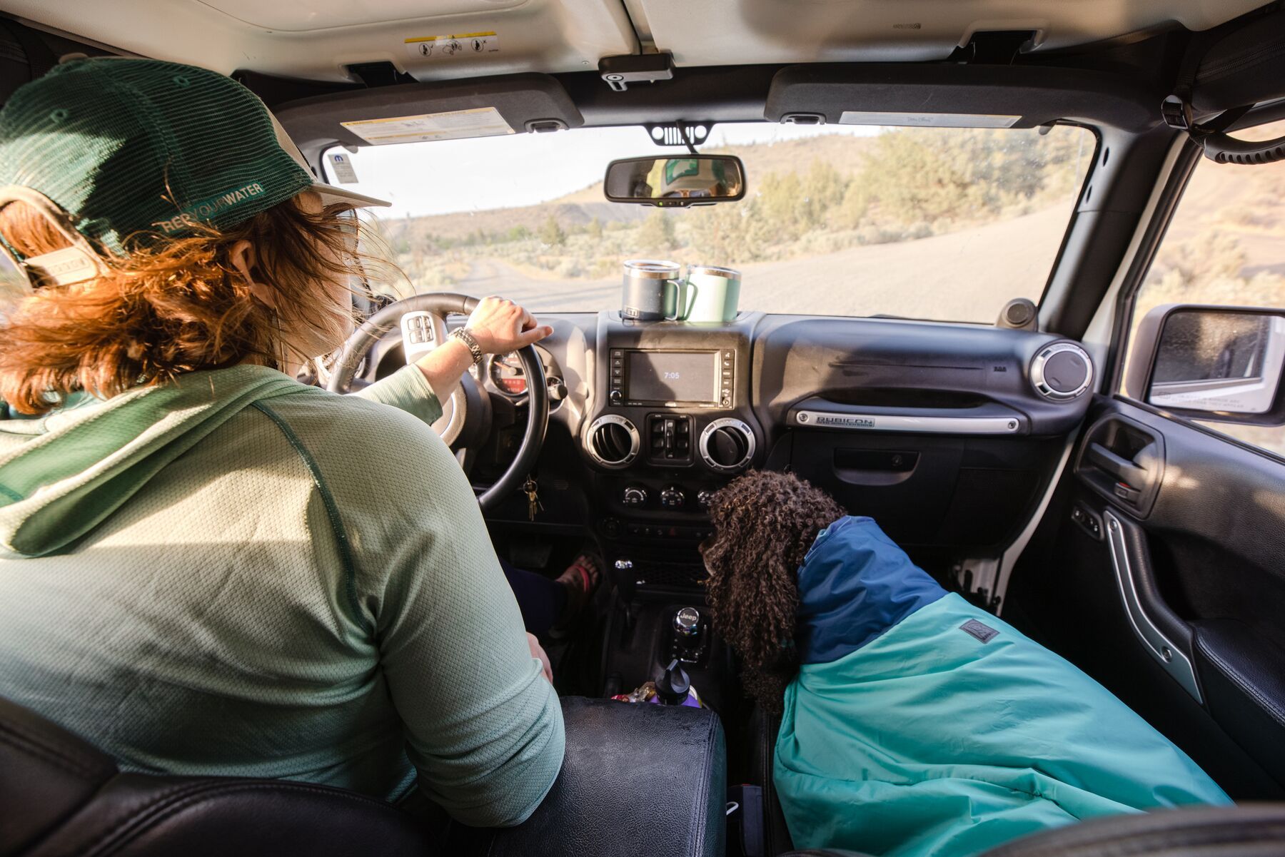 Lifestyle image of a dog wearing the Dirtbag Dog Towel, sat in the passenger seat of a car while their owner drives them.