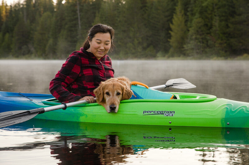 A dog and owner on a kayak, with the dog wearing the Float Coat lifejacket.